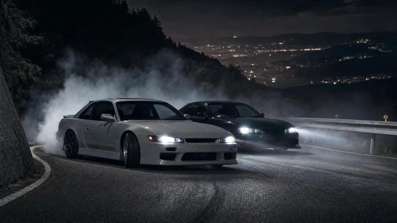 Two JDM drift cars tandem drifting with tire smoke at night