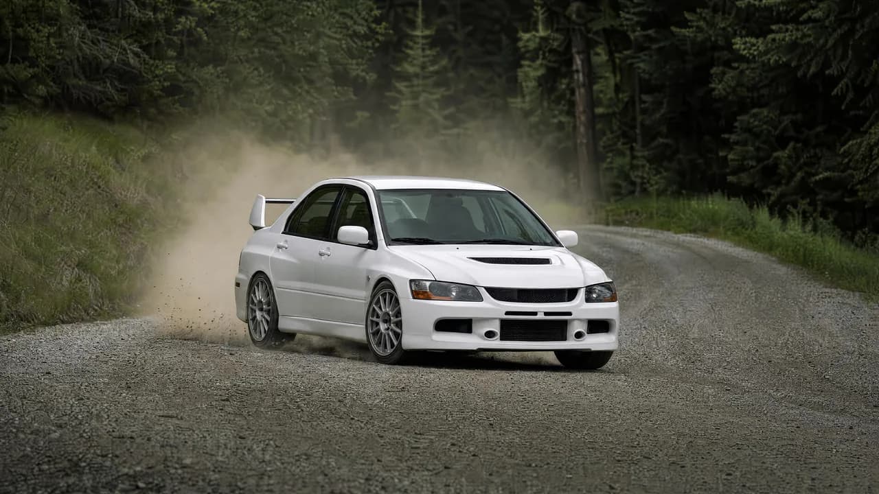 White Lancer Evo IX kicking up gravel in a forest